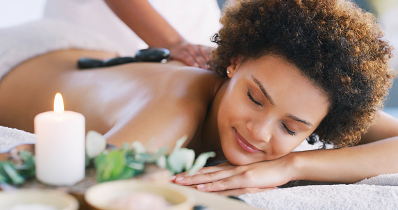 Relax, spa and zen woman for hot stone and physical therapy in room. Female client on table with candles and smile for luxury cosmetics treatment for back, health and wellness of body and mind
