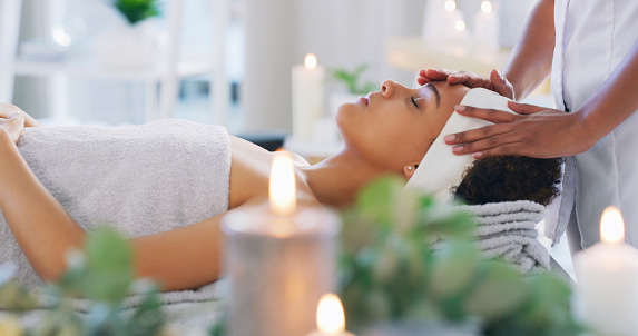 Spa, facial or head massage on a woman for beauty or skincare to relax with hands on face. Female client calm on a bed with candles and cosmetics for luxury zen treatment for health and wellness