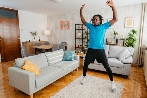 A handsome young black man working out at home. Doing jumping jacks exercise at home.