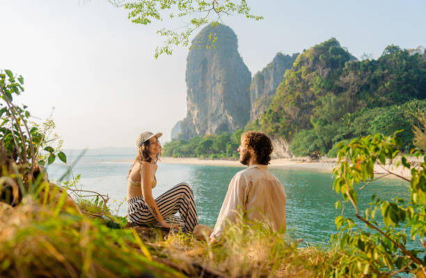 Woman and man sitting on cliff  on the background of  Railey  bay Young woman and man  sitting  and talking on cliff  on the background of  Railey  bay couple retreat stock pictures, royalty-free photos & images