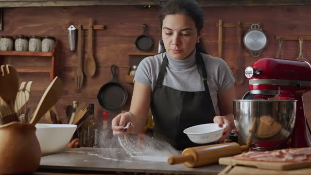 Slow motion view of Hispanic young woman spreading flour on a table for bread baking in a rustic kitchen