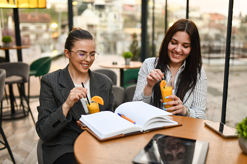 Smiling Female Financial Workers Keeping Company Log Books And Drinking Orange Juice