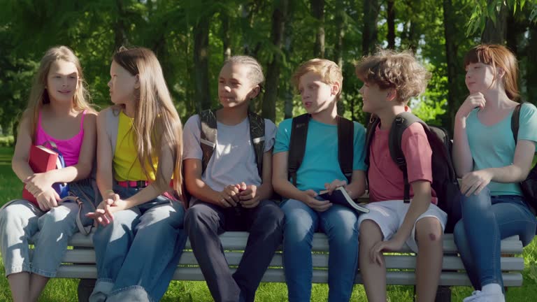 Group of friendly multiethnic kids sitting on bench in park