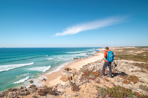 Traveller enjoys the view of the sandy beach of Praia do Malhao Sul on the Atlantic coast near Vila Nova de Milfontes, Odemira, Portugal. In the footsteps of Rota Vicentina. Fisherman trail