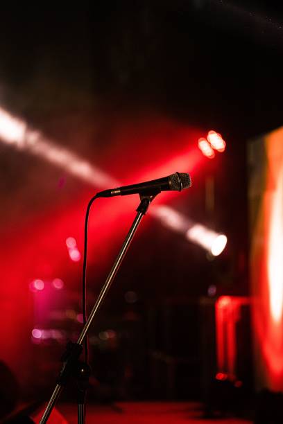 istock Professional condenser microphone resting on a stage, illuminated by a series of red stage lights 1479363230