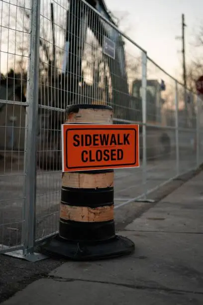 A brown metal sign attached to a black metal fence indicating the sidewalk is closed