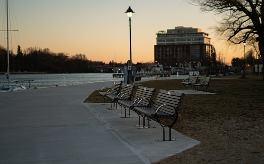 An idyllic scene of a park with a row of empty wooden benches situated along the waterfront, illuminated by the soft light of dusk