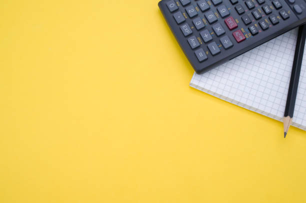 istock Partial view of a scientific calculator, pencil, and a grid notepad isolated on a yellow background 1479363994