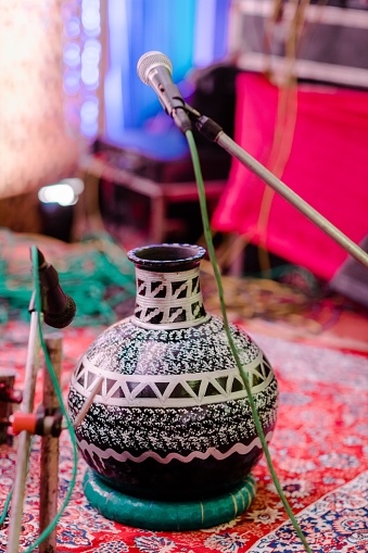 An ornate Oriental-style vase is placed atop a colorful rug with a microphone in the foreground