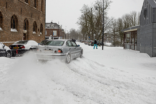 Zutphen, Netherlands – February 07, 2021: Snow splashing behind a car speeding through slippery white streets after heavy snowfall