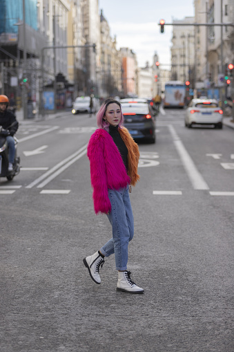 A shallow focus of a confident Hispanic woman with pink hair wearing a fluffy jacket and crossing the road