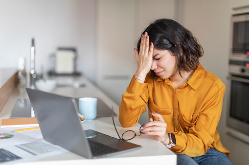 Failure Concept. Young Arab Woman Having Stress While Working With Laptop Computer At Home, Depressed Middle Eastern Female Freelancer Sitting At Kitchen Counter, Having Problems With Remote Work