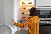 Unrecognizable Young Woman Opening Fridge In Kitchen And Looking Inside