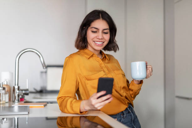 istock Online Communication. Young Arab Woman Using Smartphone And Drinking Coffee In Kitchen 1479370112