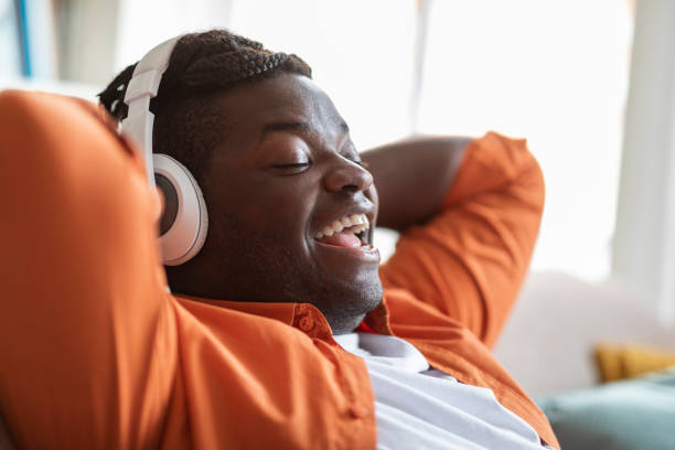 istock Positive black guy reclining on sofa, singing songs, using headphones 1479370145