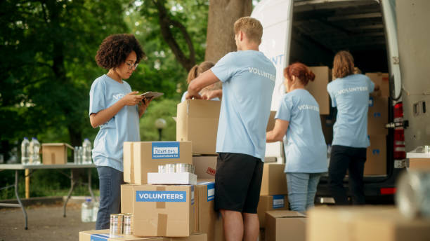 istock Group of Hardworking Volunteers Preparing Donated Free Food Rations, Loading Packages in a Cargo Van on a Sunny Day. Charity Workers Work in Local Humanitarian Aid Organization. 1479370967