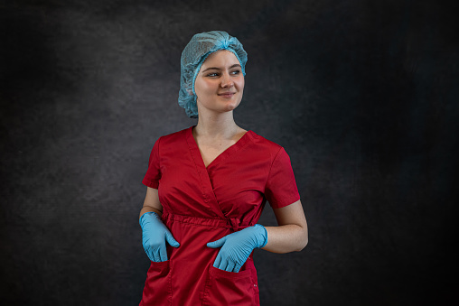 Portrait of nurse wearing red scrub standing with arms crossed on studio gray background with copy space advertising area