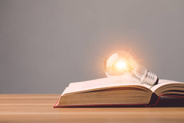 istock Close up clear light bulb with light effect on old book and put on wooden desk with grey space wall background. Idea of learning, Education concept. 1479370990