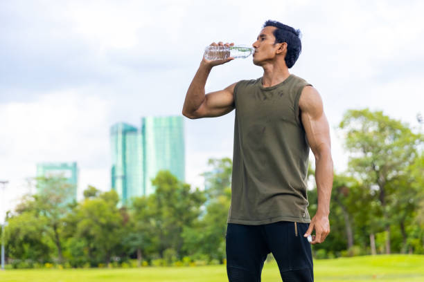 Asian man drinking water during jogging exercise at park in the morning.
