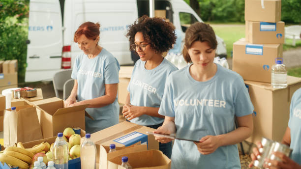 group of volunteers preparing free food rations for poor people in need. charity workers and members of the community work together. concept of giving, humanitarian aid and society. - voluntário imagens e fotografias de stock