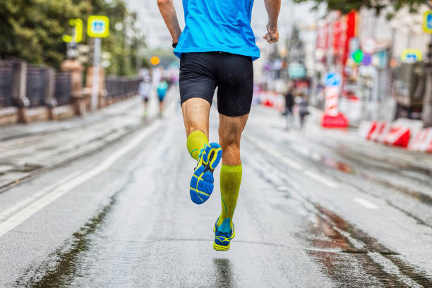 volta atleta masculino em meias de compressão correndo maratona na cidade, corrida esportiva de verão, correndo no asfalto molhado após a chuva - passadeira via pública - fotografias e filmes do acervo