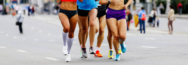 les coureuses de groupe courent le marathon. jambes élancées filles course en ville, événement sportif d’été - marathon running motion track event photos et images de collection