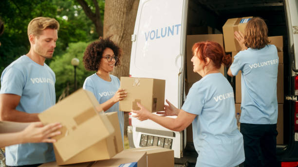 istock Happy Team of Young Volunteers Preparing Humanitarian Aid and Donations, Loading Cardboard Boxes in a Cargo Van Outdoors. Charity Workers Work in Humanitarian Donation Center 1479372949