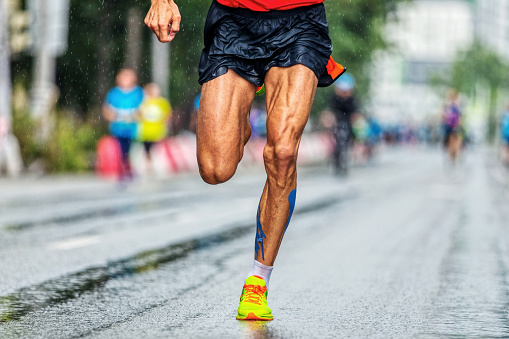 close-up muscular legs male runner running marathon city race, athlete run on wet asphalt after rain