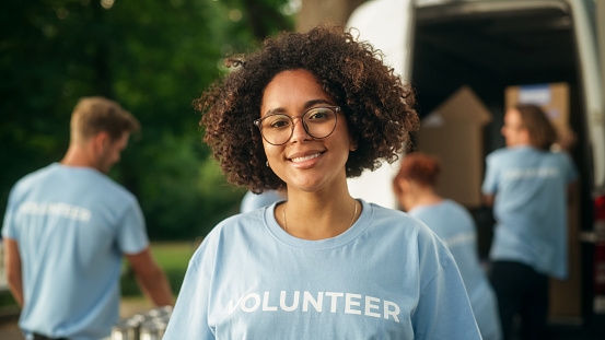 Portrait of a Happy Helpful Black Female Volunteer. Young Adult Multiethnic Latina with Afro Hair, Wearing Glasses, Smiling, Posing for Camera. Humanitarian Aid and Volunteering Concept.