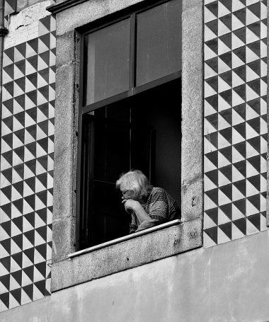 Porto, Portugal – July 21, 2022: Elderly woman seated at window gazing outwardly