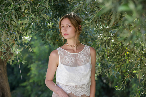 Fashion portrait of woman in white lace top with greenery behind, summer vacation fashion