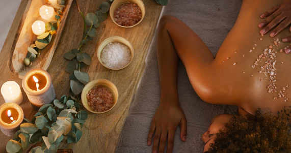 Back, spa and salt scrub massage on woman with candles for zen, physical therapy or skincare. A female relax with therapist hands on skin for cosmetics or luxury treatment for health and wellness