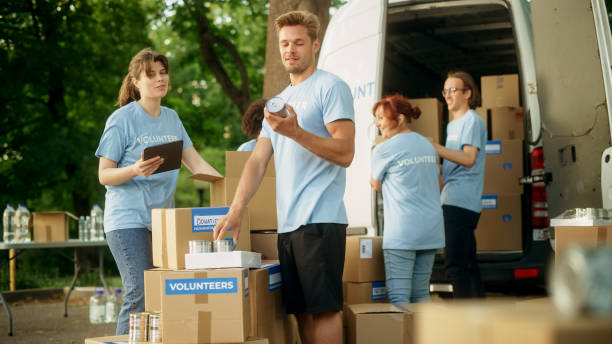 istock Team of Young Volunteers Preparing Humanitarian Aid Rations, Food, Donations and Loading Packages in a Van on a Sunny Day. Charity Workers Work in Humanitarian Donation Center. 1479376744