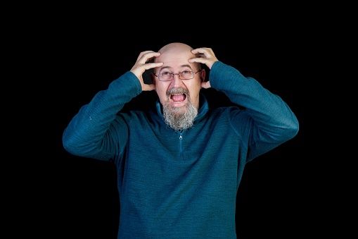A middle-aged man in a state of discomfort, isolated against a black background, holding his head as if suffering from a severe headache or migraine