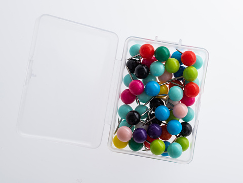 Plastic box with colorful pins on white background
