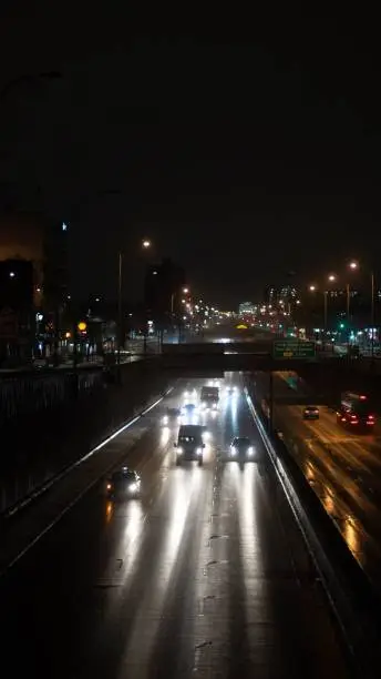 A vertical shot of a line of cars are illuminated in the darkness of night at the Queen Mary Street in Montreal