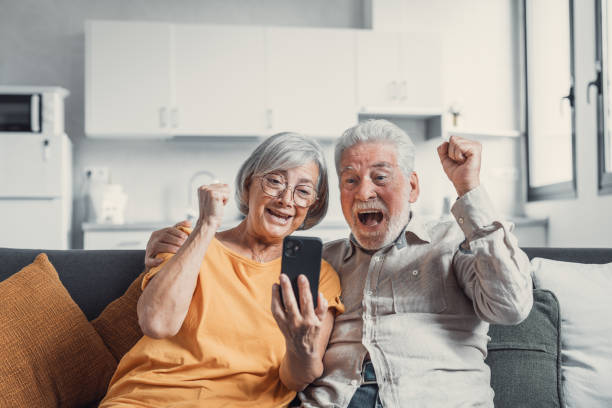 istock Happy older couple sit on couch staring at cellphone screen gesturing looking overjoyed, scream with joy, read fantastic news, get great commercial offer, pension raise. Success, achievement concept 1479384610