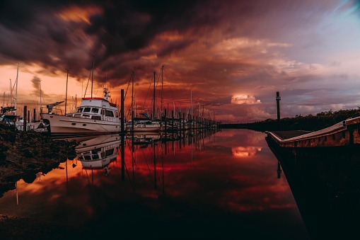 An ominous landscape featuring multiple boats, illuminated by the orange hues of the sunset