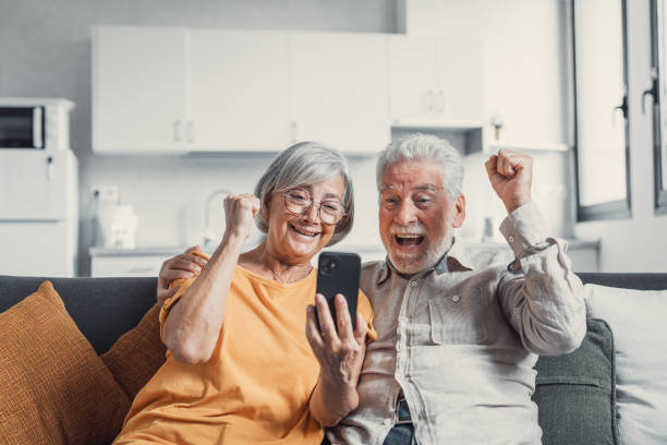 istock Happy older couple sit on couch staring at cellphone screen gesturing looking overjoyed, scream with joy, read fantastic news, get great commercial offer, pension raise. Success, achievement concept 1479386351