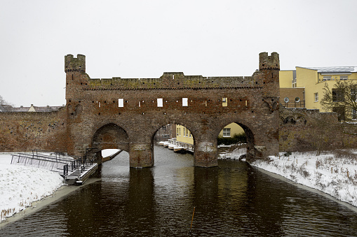 Medieval Hanseatic city wall during a snowstorm showing remains of the Berkelpoort with the white snow and river Berkel in the foreground