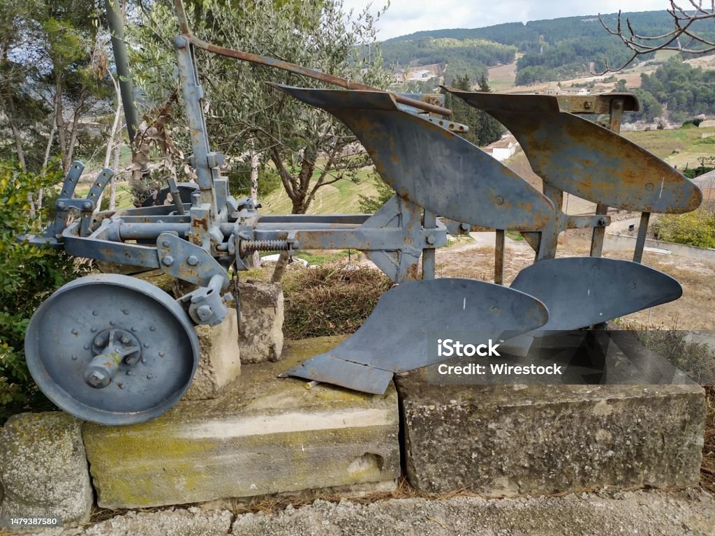 a steel plow in the front of a house with trees and grass A steel plow is situated in the front yard of a rural home surrounded by trees and lush green grass Agricultural Field Stock Photo