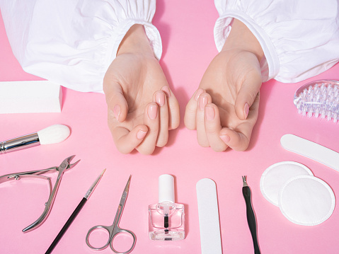 Primer plano del salón de uñas de manos femeninas bien cuidadas y uñas recién cuidadas con fondo rosa. Concepto de la industria de la belleza y el cuidado con herramientas de manicura, como tijeras, pinzas y pinzas. photo