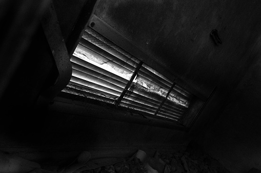Atmospheric greyscale image of an antique window with blinds closed, creating a moody atmosphere