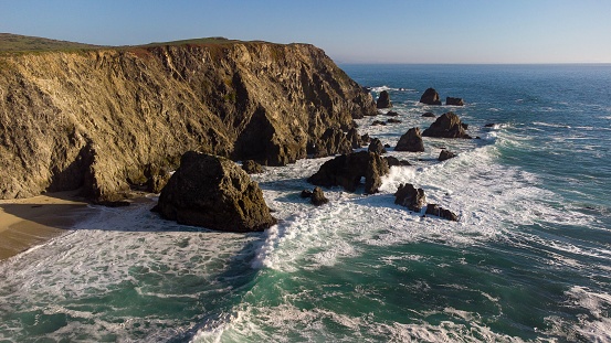 An aerial shot of Bodega Bay in California with big waves crashing into the rocks during golden hour.