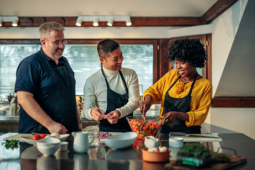 A young diverse couple is in their kitchen having a cooking class with a chef.