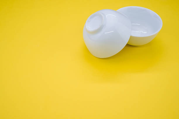 istock Closeup of two empty white bowls on a yellow background with space for your text 1479412522