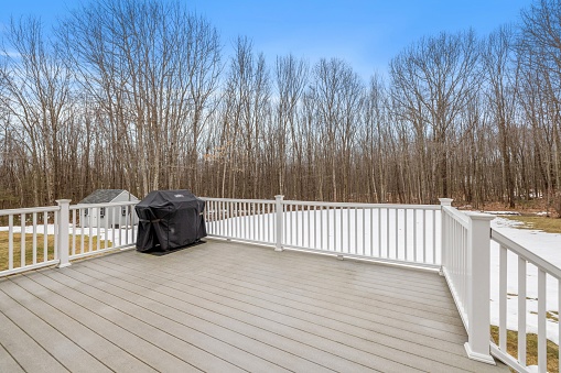 An outdoor patio area featuring a large wooden deck with bared trees in the background