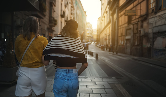 Two women are walking around the summer city. Back view.