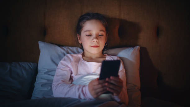 istock Small Girl Using Smartphone in Bed Before Going to Sleep. Cute Kid Checking Social Media, School Schedule, Reading Homework on Digital Ebook, Chatting with Friends Online. 1479421215