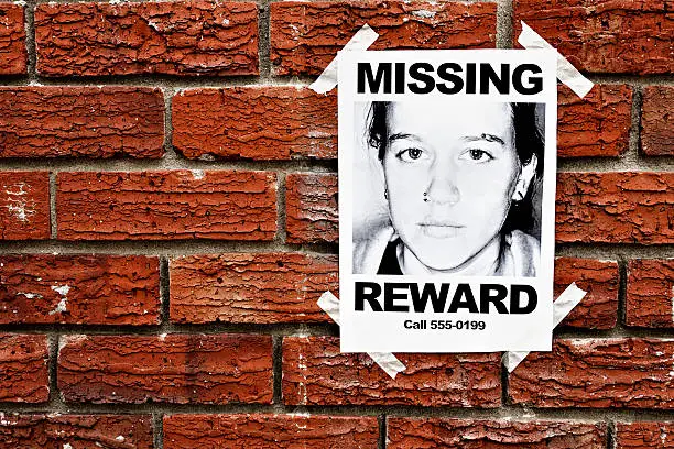 A "Missing" poster of a teenage girl, offering a reward,  is taped to a red brick wall, possibly in a police station. The phone number is a "555" dummy following the Hollywood convention. Please see http://en.wikipedia.org/wiki/555_%28telephone_number%29